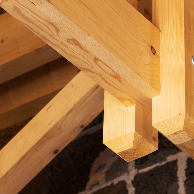 Charpente bois traditionnelle : Structure et ossature de toiture Charpente bois neuve symétrique. Ossature de toiture en poutres et chevrons s'élevant vers la faîtière, fond de ciel nuageux.