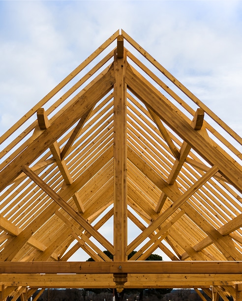 Charpente bois traditionnelle : Structure et ossature de toiture Charpente bois neuve symétrique. Ossature de toiture en poutres et chevrons s'élevant vers la faîtière, fond de ciel nuageux.