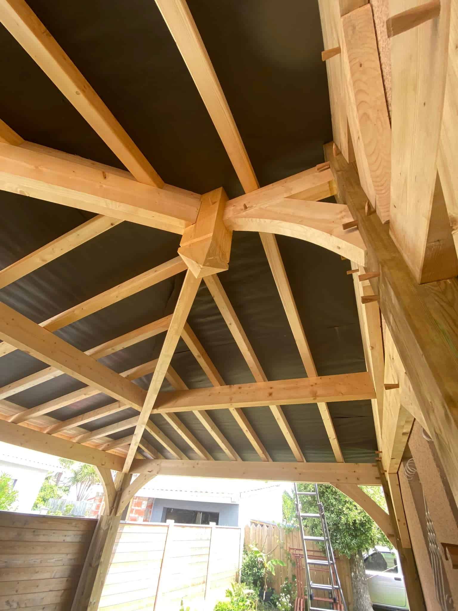 Charpente bois traditionnelle : Structure et ossature de toiture Charpente bois neuve symétrique. Ossature de toiture en poutres et chevrons s'élevant vers la faîtière, fond de ciel nuageux.