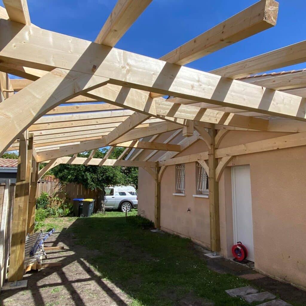 Construction d'une Charpente de Pergola en Bois Massif Charpente de pergola en bois massif en cours de construction contre une maison, avec poutres et chevrons apparents.