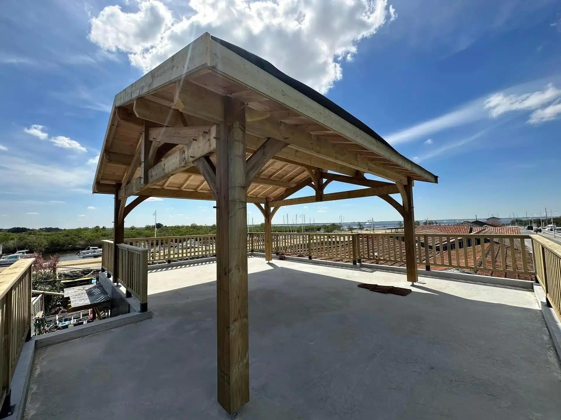 Charpente bois traditionnelle : Structure et ossature de toiture Charpente bois neuve symétrique. Ossature de toiture en poutres et chevrons s'élevant vers la faîtière, fond de ciel nuageux.