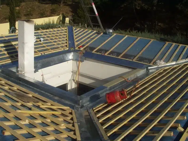 Charpente bois traditionnelle : Structure et ossature de toiture Charpente bois neuve symétrique. Ossature de toiture en poutres et chevrons s'élevant vers la faîtière, fond de ciel nuageux.