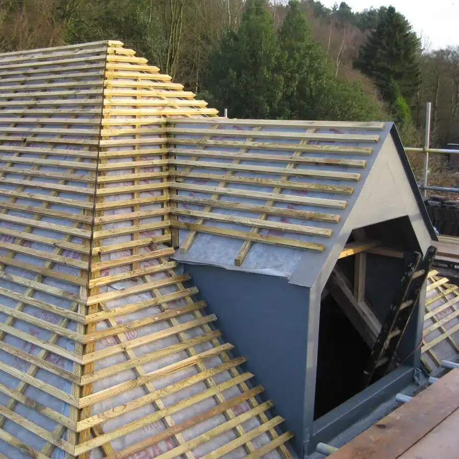 Toiture en Construction : Pose des Liteaux et Lucarne Pose de liteaux en bois sur membrane de sous-toiture et lucarne grise d'un toit en construction.