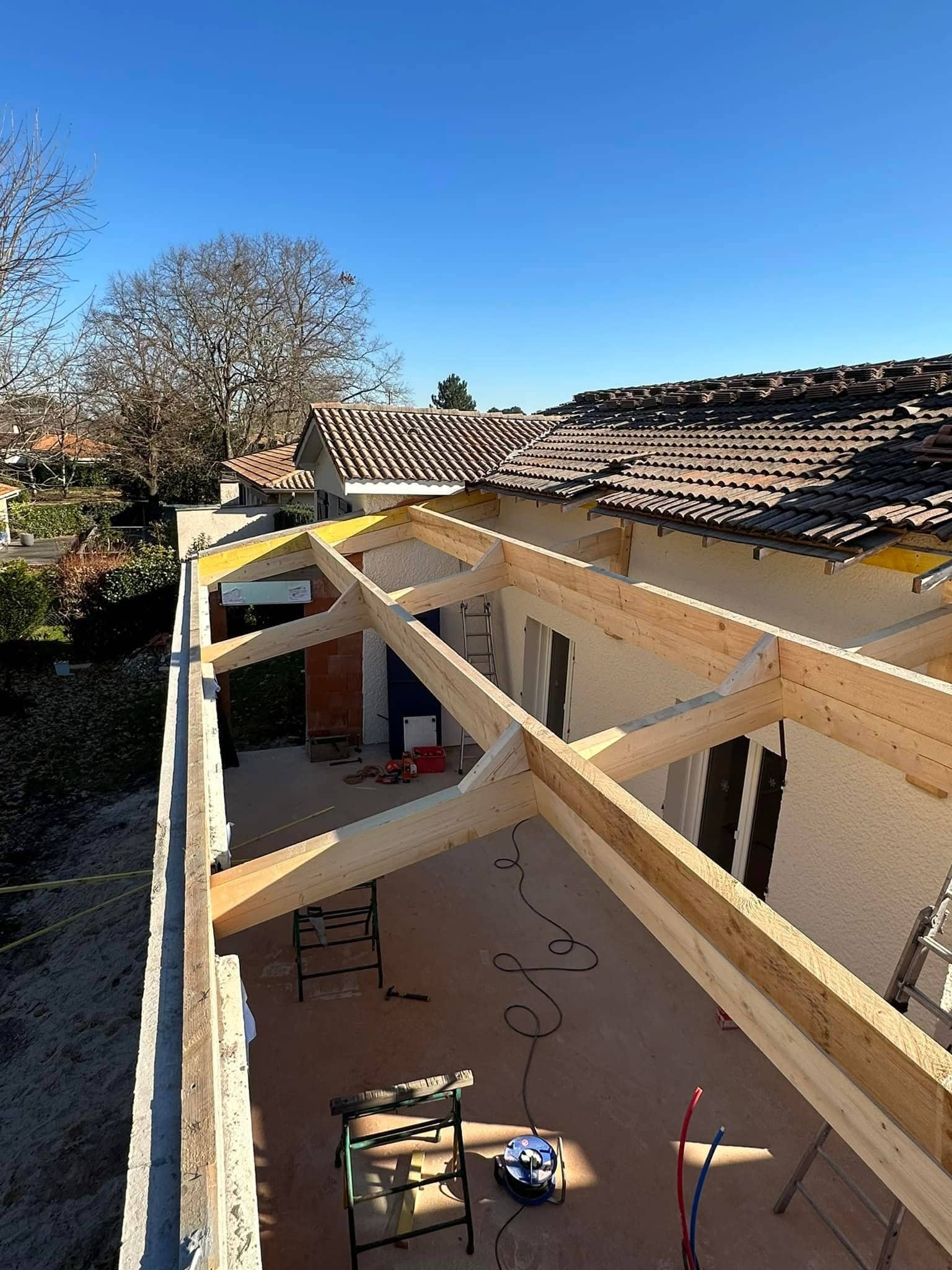Construction d'une charpente en bois pour l'extension de toiture d'une maison sous un ciel bleu.