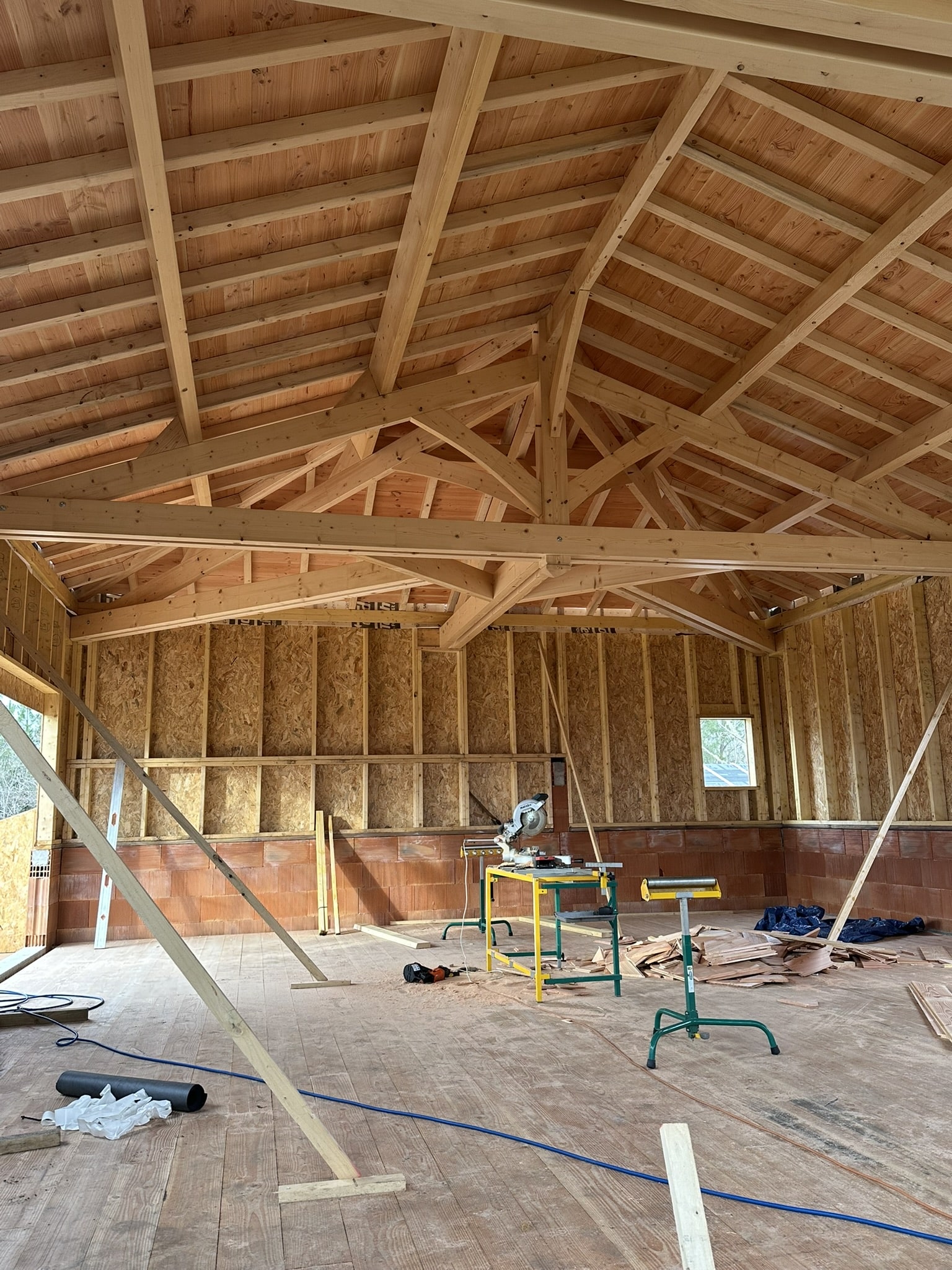 Intérieur d'un bâtiment avec charpente en bois apparente, murs OSB et outils de menuiserie sur un chantier.