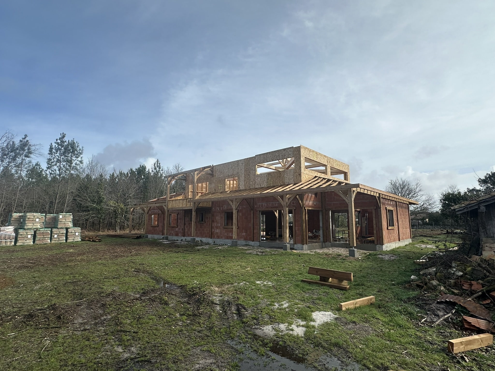 Maison individuelle en briques rouges avec étage en ossature bois sur un chantier de construction ensoleillé.