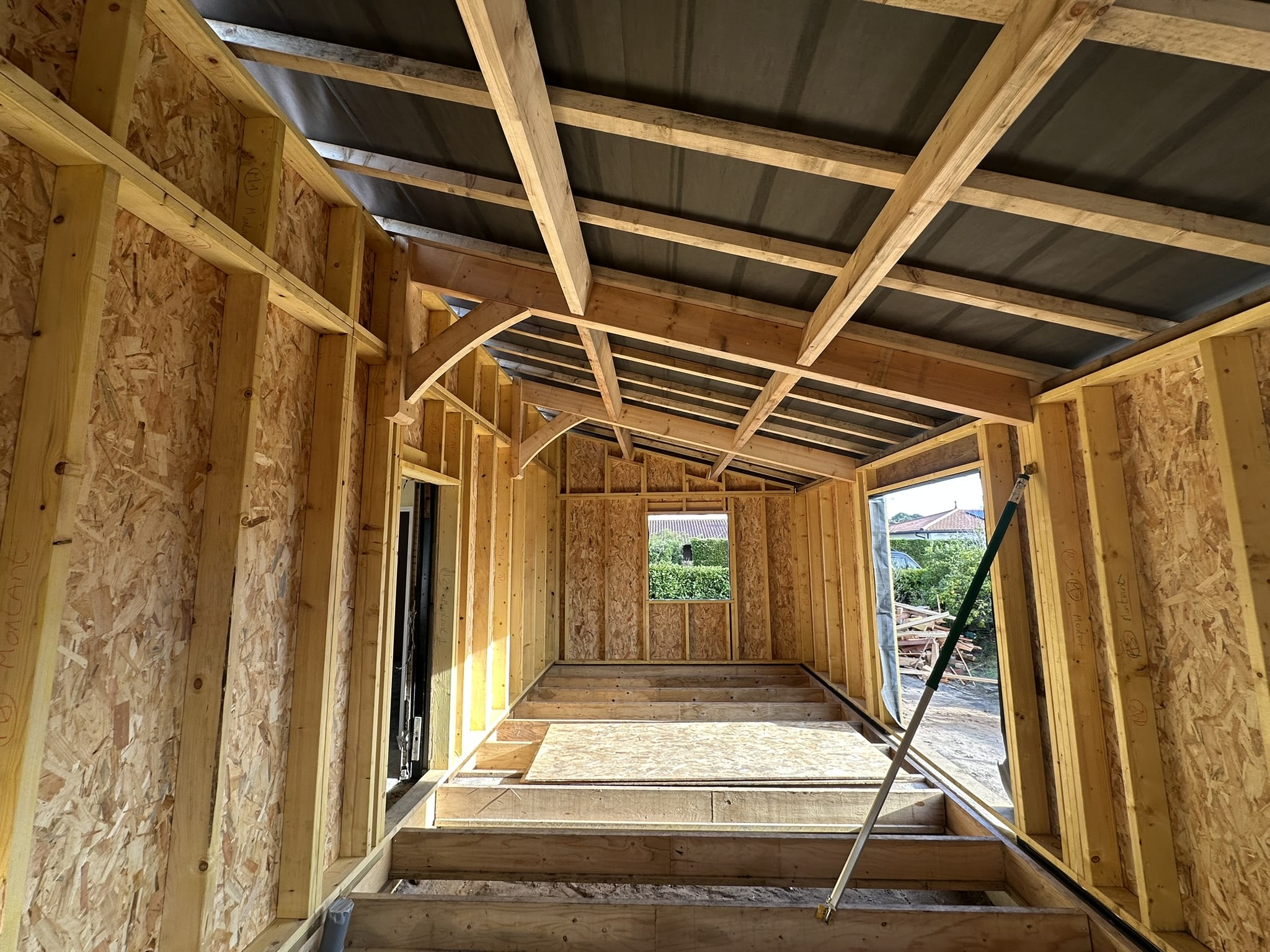 Intérieur d'une extension en ossature bois avec murs en OSB et charpente apparente sous un toit incliné en chantier.
