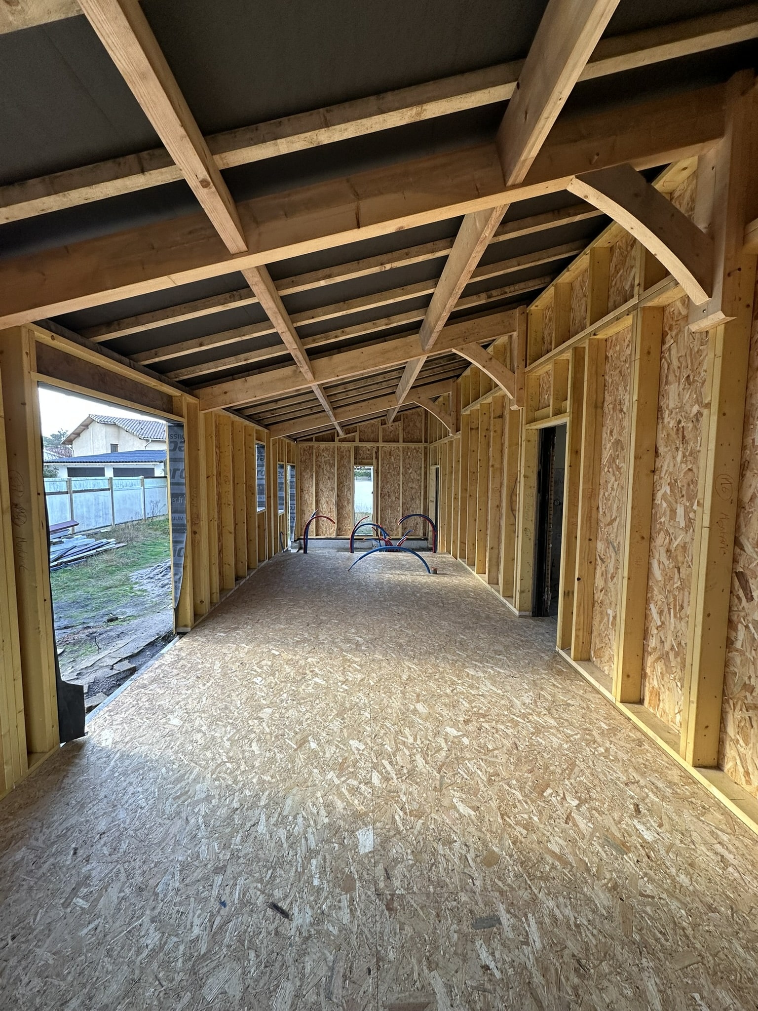 Chantier d'extension en bois avec sol OSB, charpente apparente et gaines de plomberie intégrées.