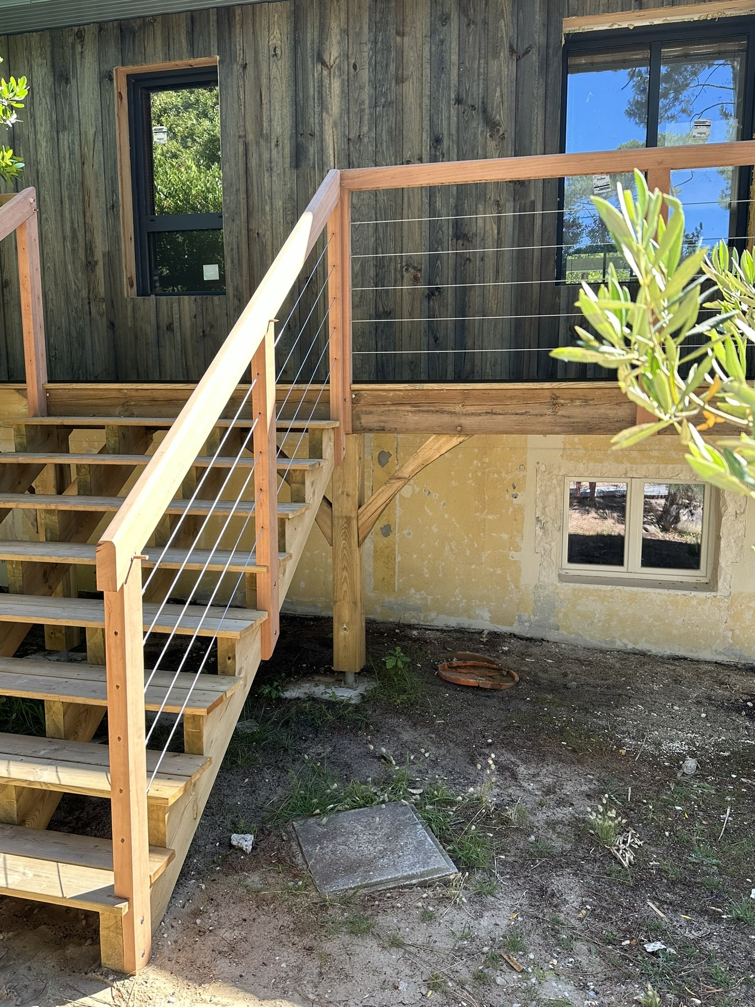 Escalier et garde-corps en bois massif avec câbles en inox bordant une terrasse moderne sur une façade en bois brûlé.