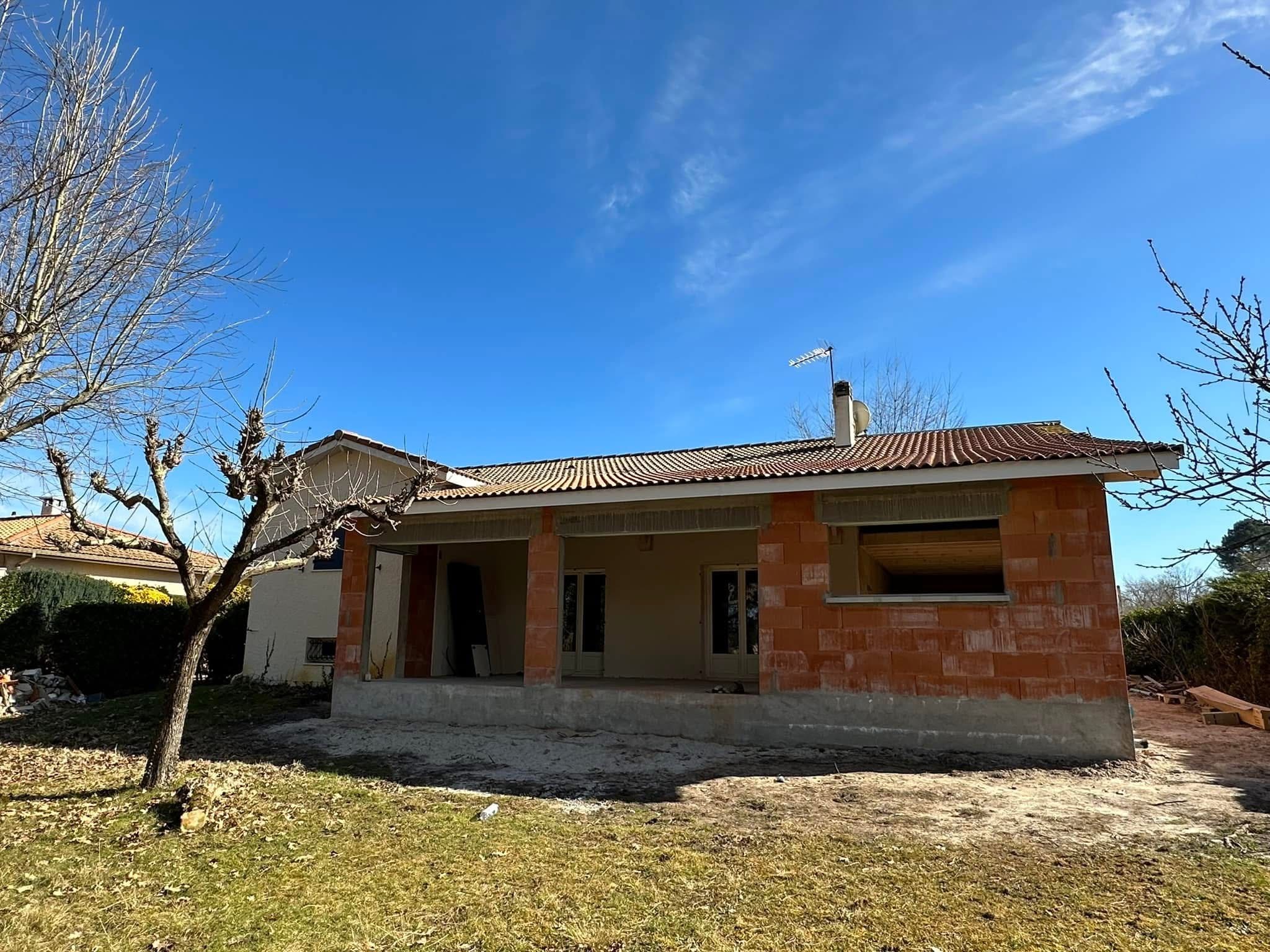 Extension de maison en briques rouges avec toit de tuiles sur un chantier de rénovation extérieur.