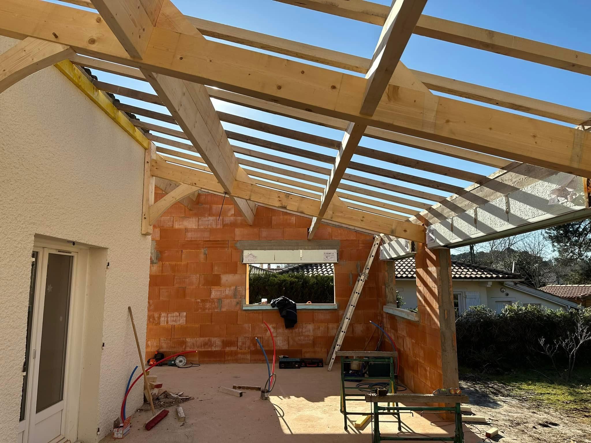 Charpente bois d'une extension de maison en briques rouges sous un ciel bleu dégagé lors d'un chantier de construction.