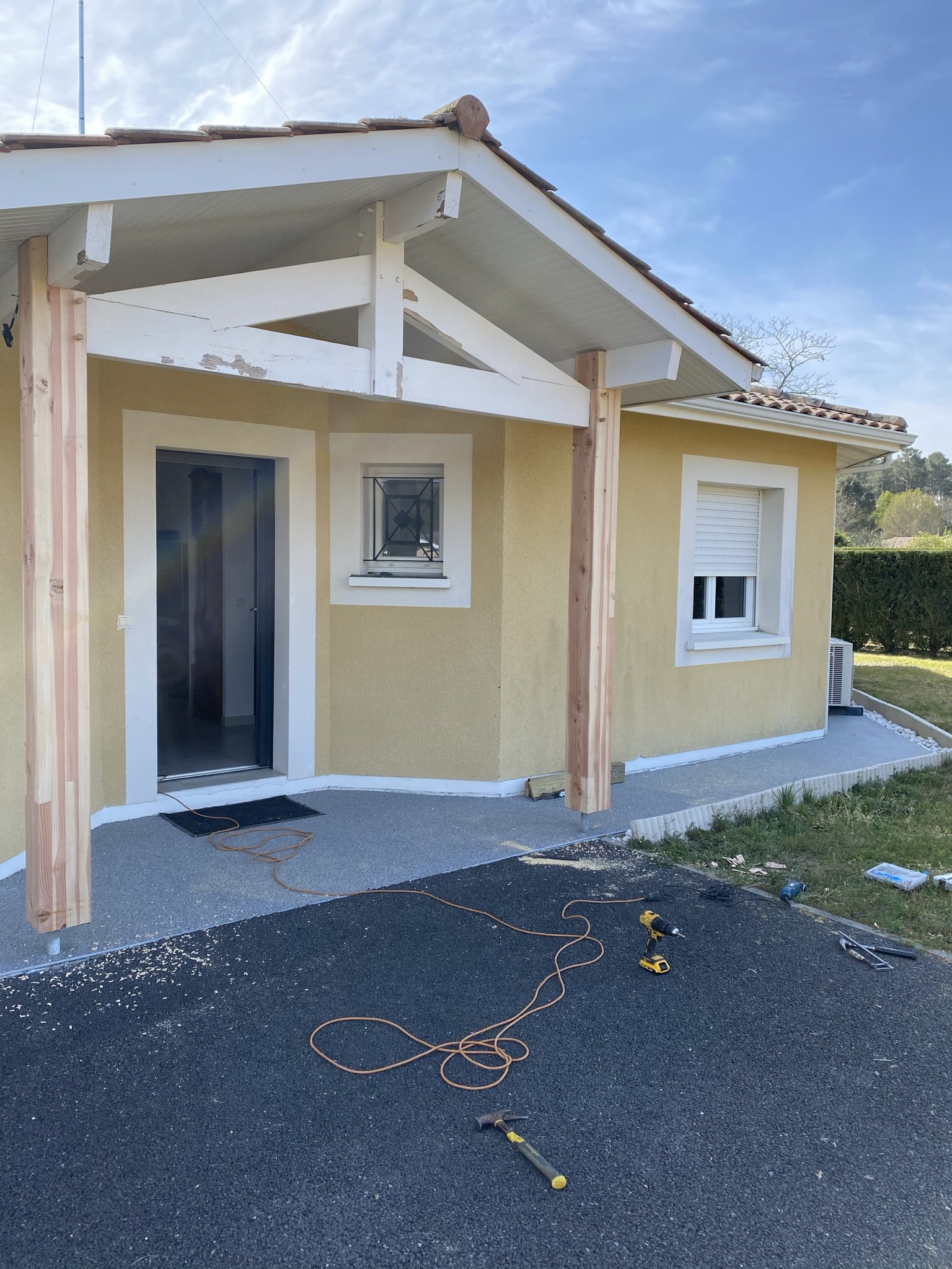 Rénovation d'un porche de maison avec nouveaux poteaux en bois et façade jaune, travaux en cours.