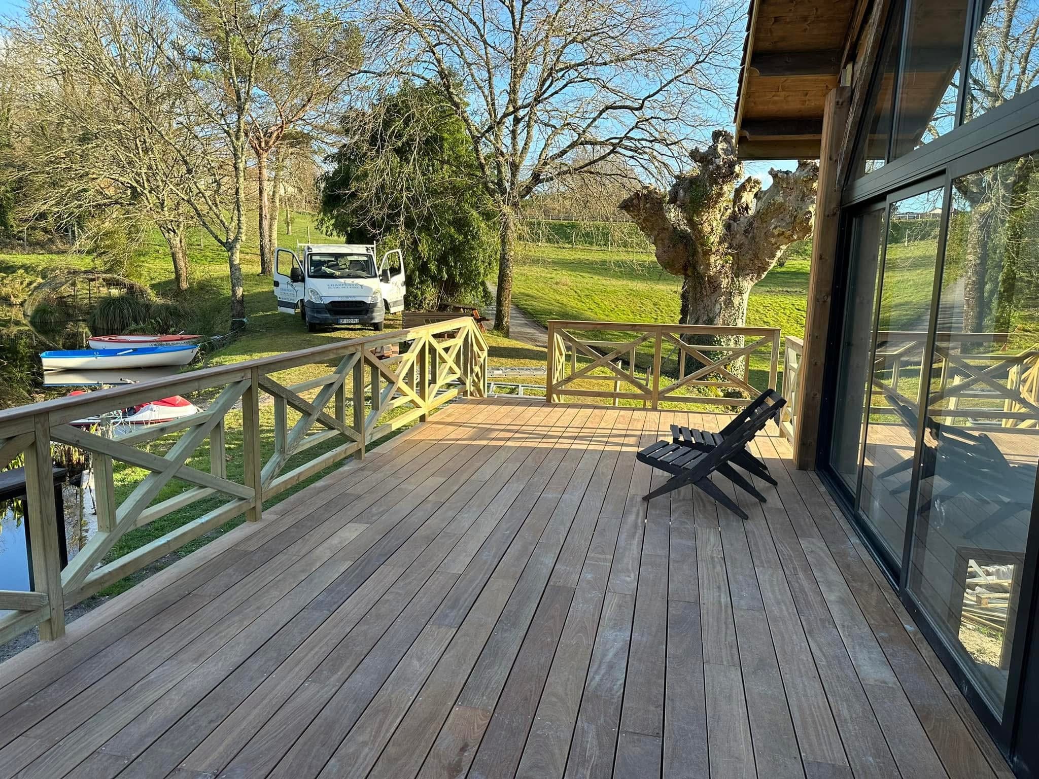 Terrasse en bois paisible avec vue sur lac, barques et camionnette Charpente du Lac au soleil.