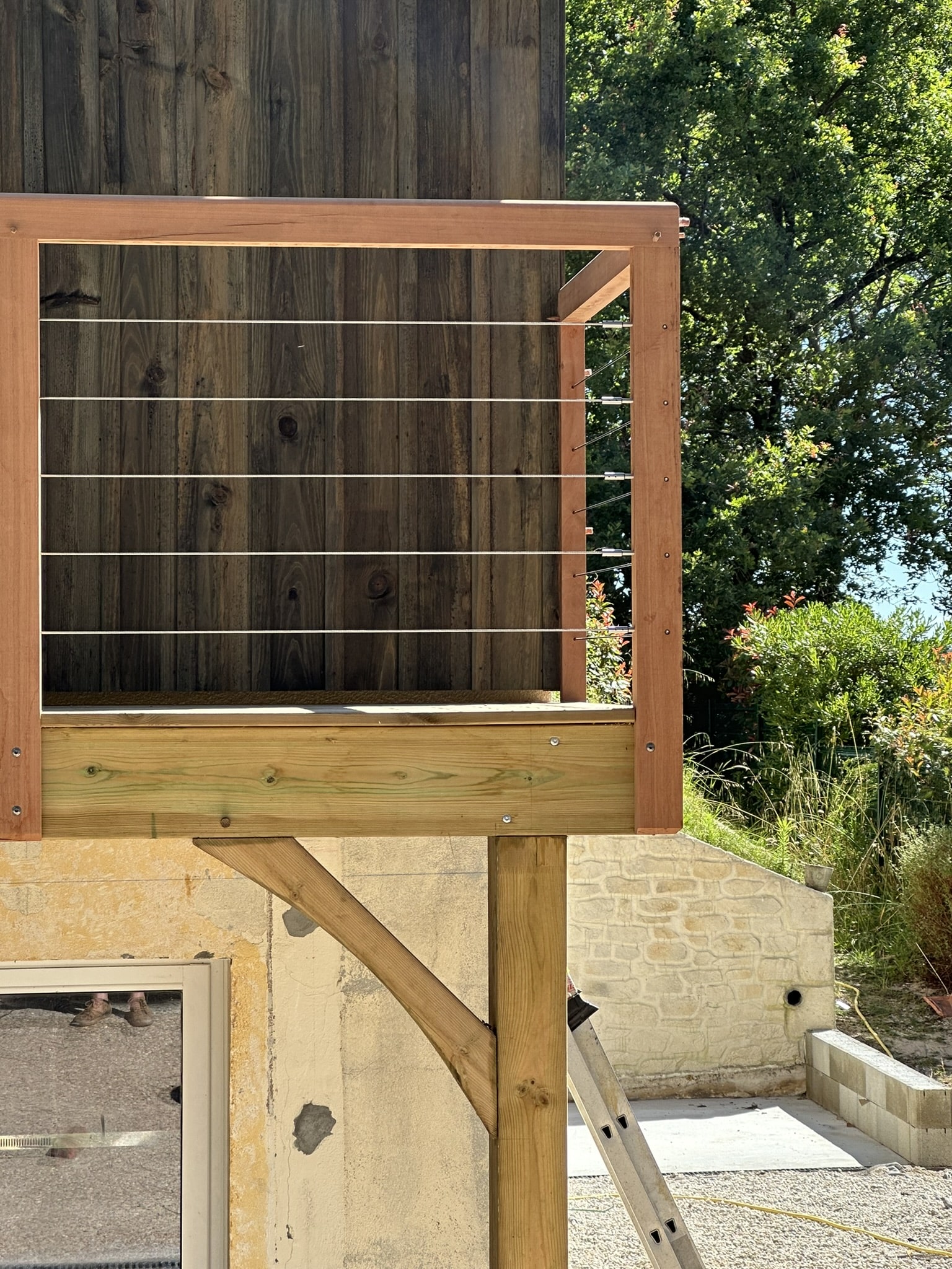 Garde-corps à câbles inox et poteaux en bois sur une terrasse moderne avec bardage sombre.