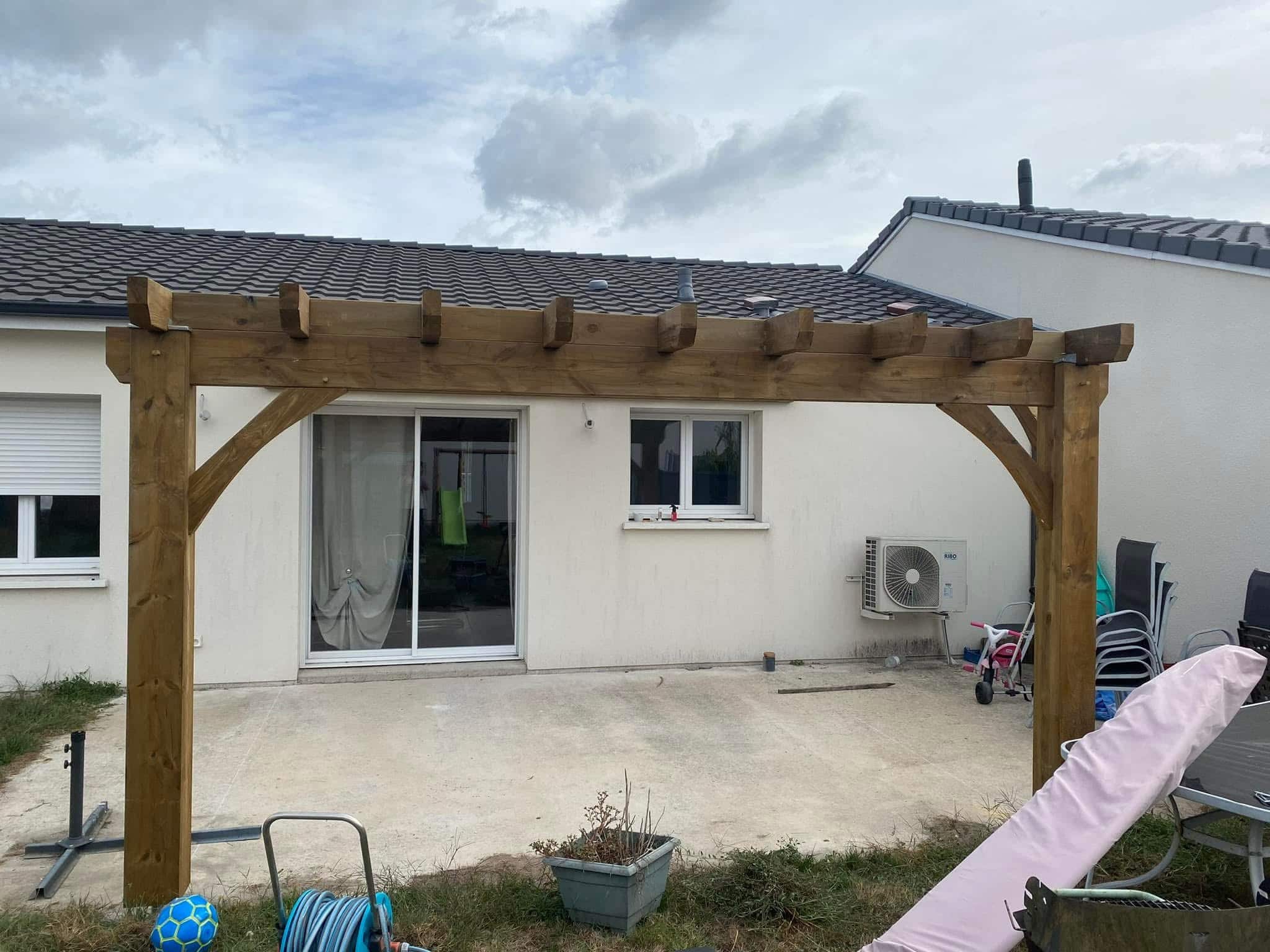 Pergola en bois sur terrasse en béton devant une maison moderne avec baie vitrée.