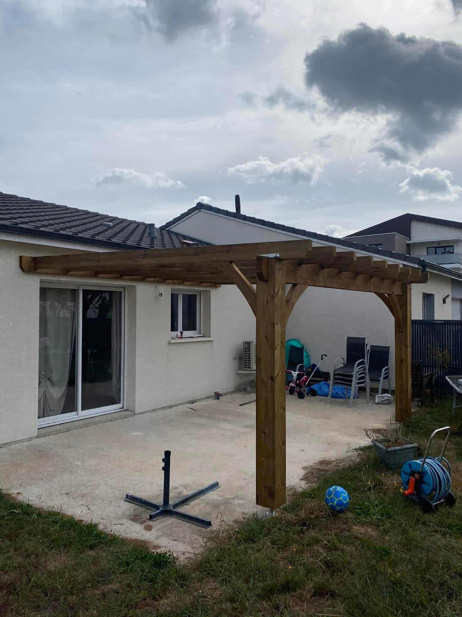Pergola en bois sur terrasse béton adossée à une maison moderne.