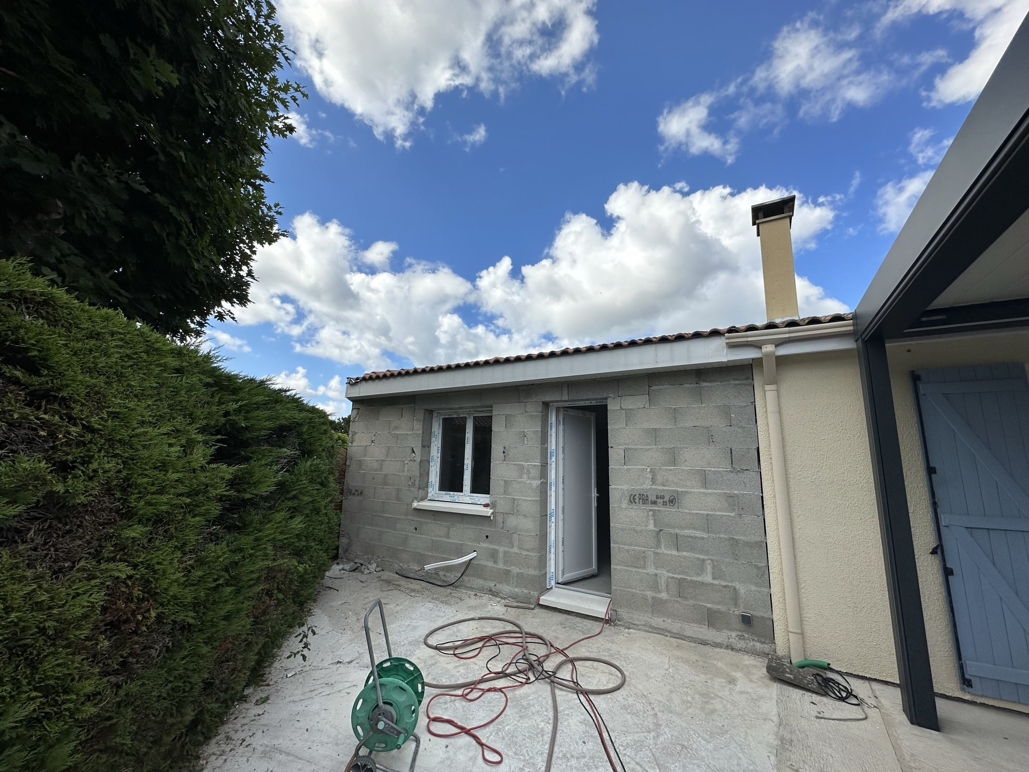Chantier d'extension de maison en parpaings avec menuiseries blanches.